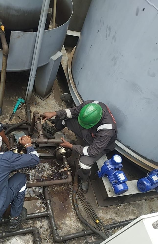 Crew replacing transfer pumps beside vertical storage tanks